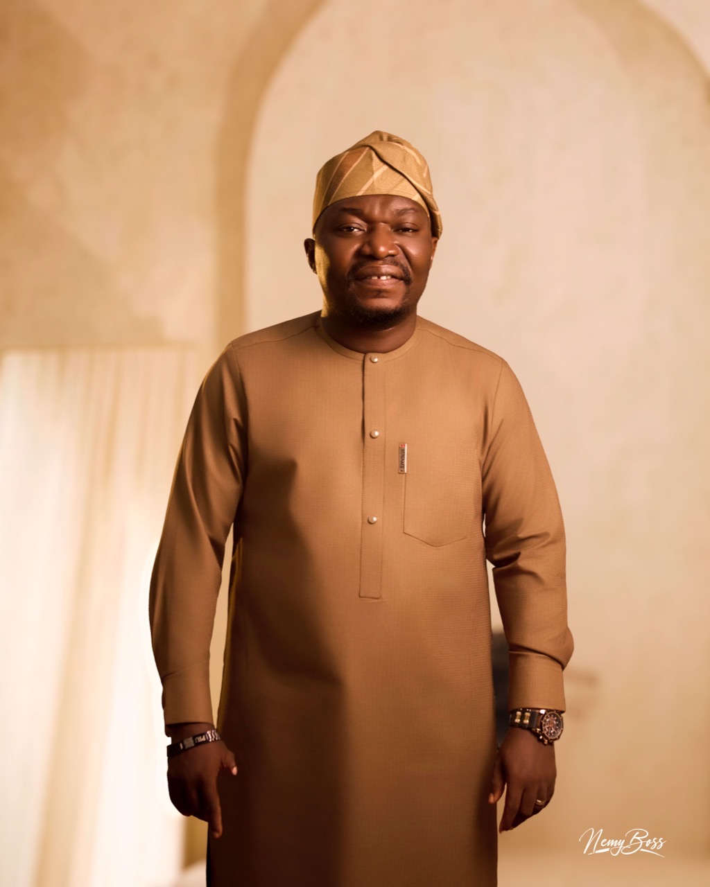 Pastor Ifeanyi Uwakwe in a tan kaftan and matching cap, before a pale archway.