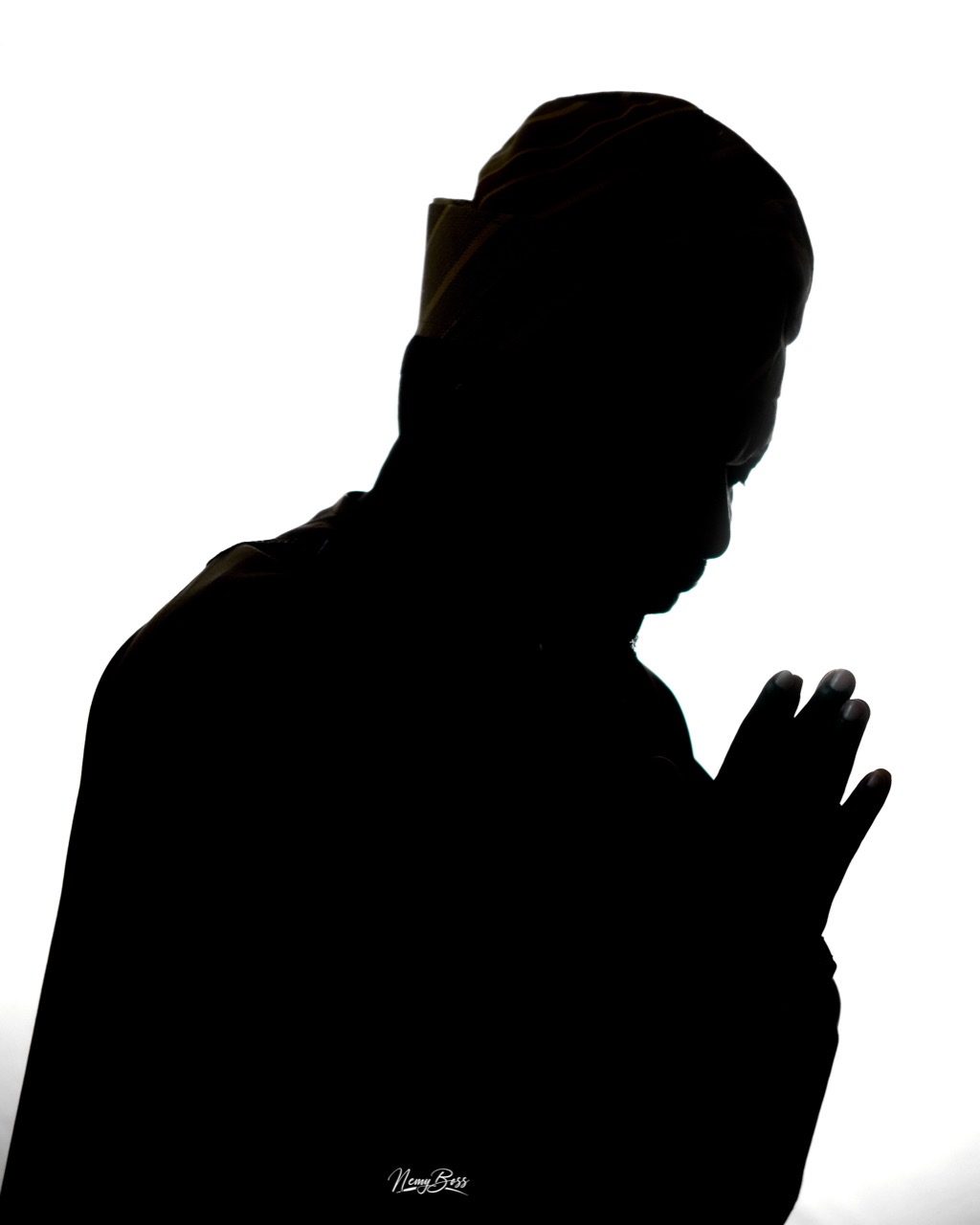 Pastor Ifeanyi Uwakwe in silhouette against a bright ground, head bowed and hands raised in prayer.